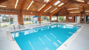An indoor swimming pool with wooden beams, clear glass walls, and a blue pool. - Ski Harbor 16 by Taylor Made Deep Creek (McHenry)