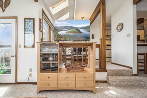 A living room with a wooden cabinet, a television displaying a landscape, and a dining area with a table and chairs. - Ski Harbor 16 by Taylor Made Deep Creek (McHenry)