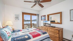 Ein Schlafzimmer mit einem großen Bett, einer Holzkommode, einem Deckenventilator, einem Fernseher und einem Fenster mit Seeblick.
