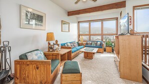Un salon chaleureux avec une grande fenêtre, des meubles en bois et un ventilateur de plafond.