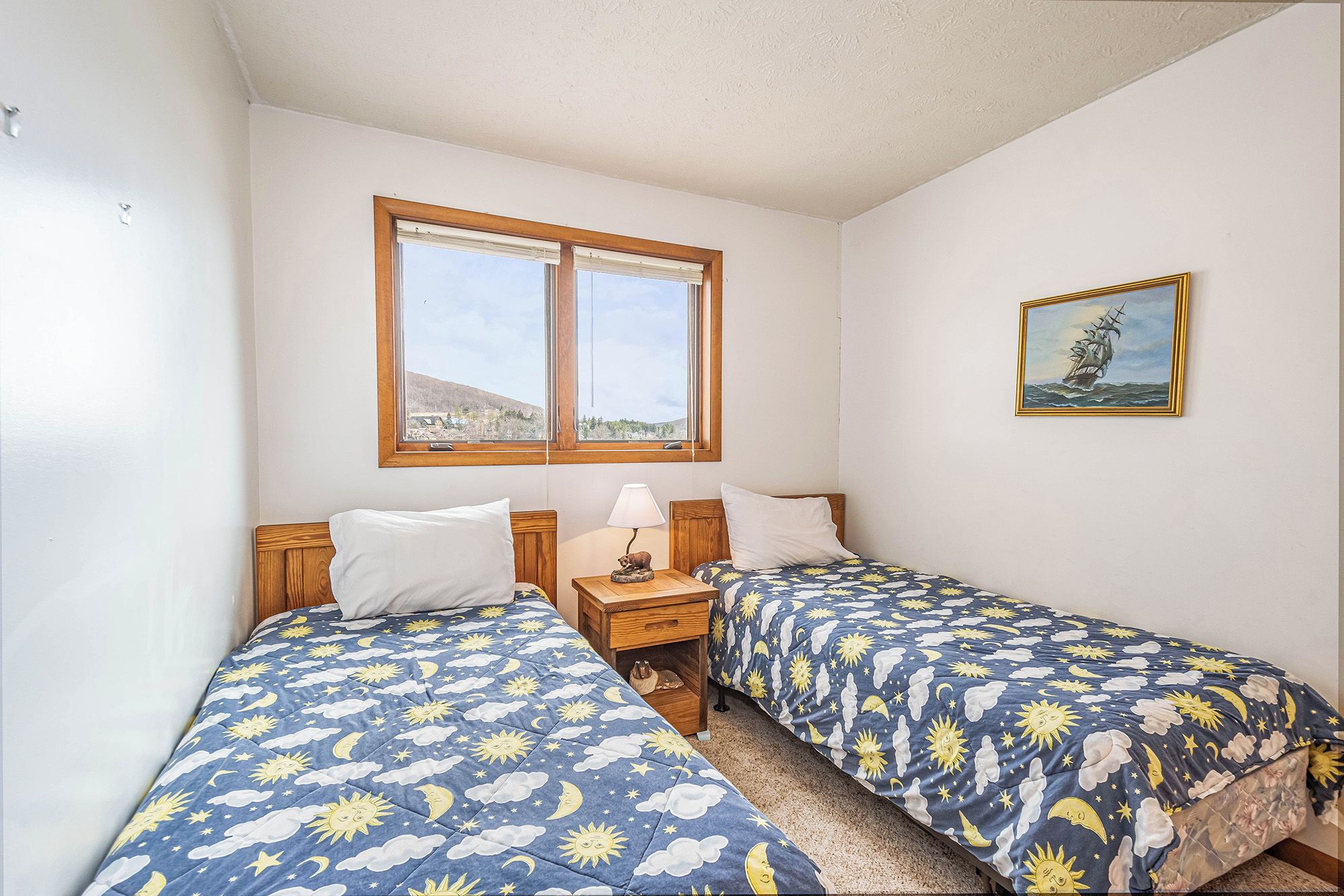 A bedroom with two beds, a window, and a painting.