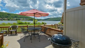 Eine Terrasse mit Tisch, Stühlen, einem Grill und Blick auf einen See.