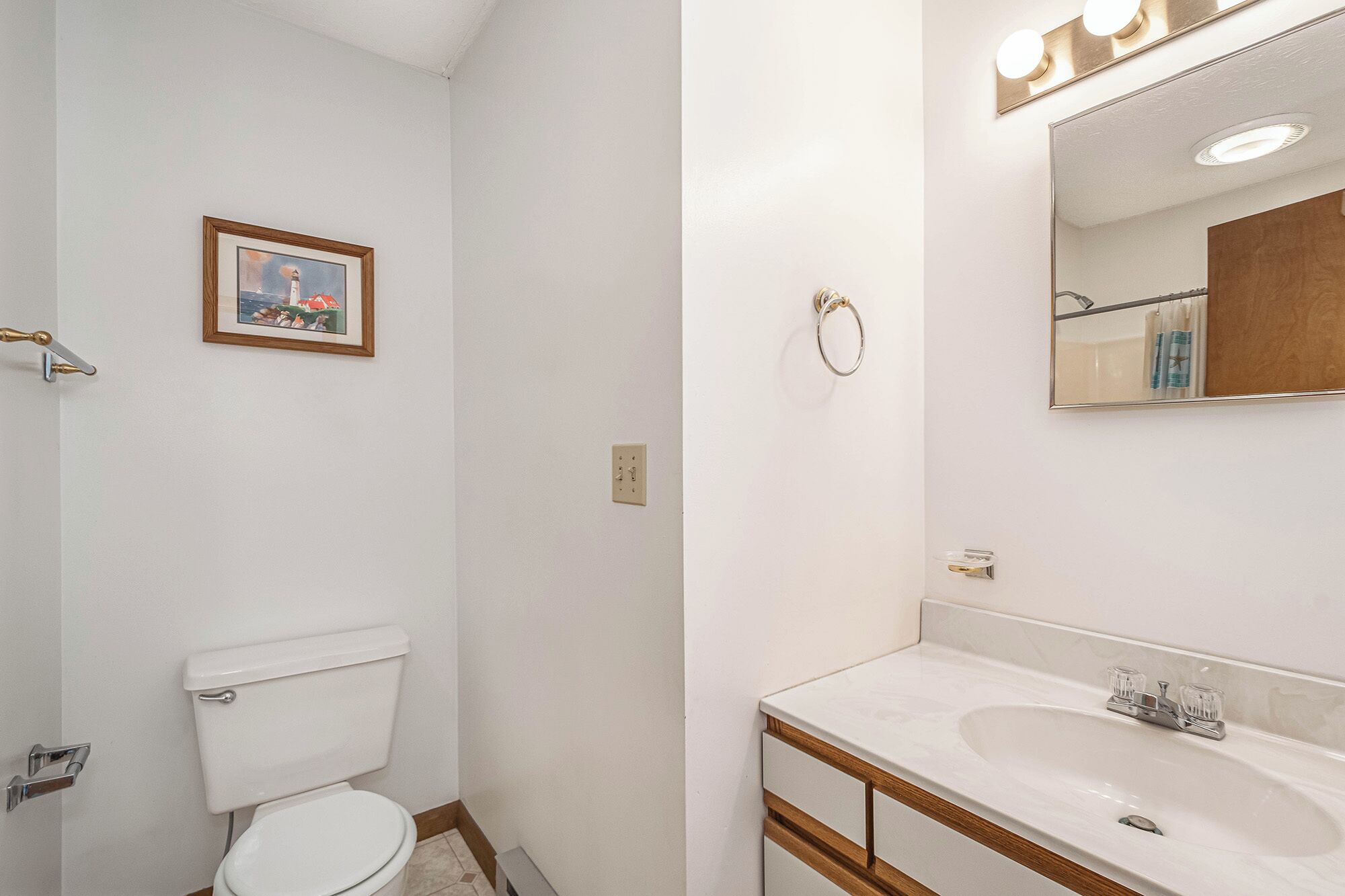 Une salle de bain avec des toilettes, un lavabo, un miroir et un tableau encadré au mur.