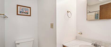 Une salle de bain avec des toilettes, un lavabo, un miroir et un tableau encadré au mur.
