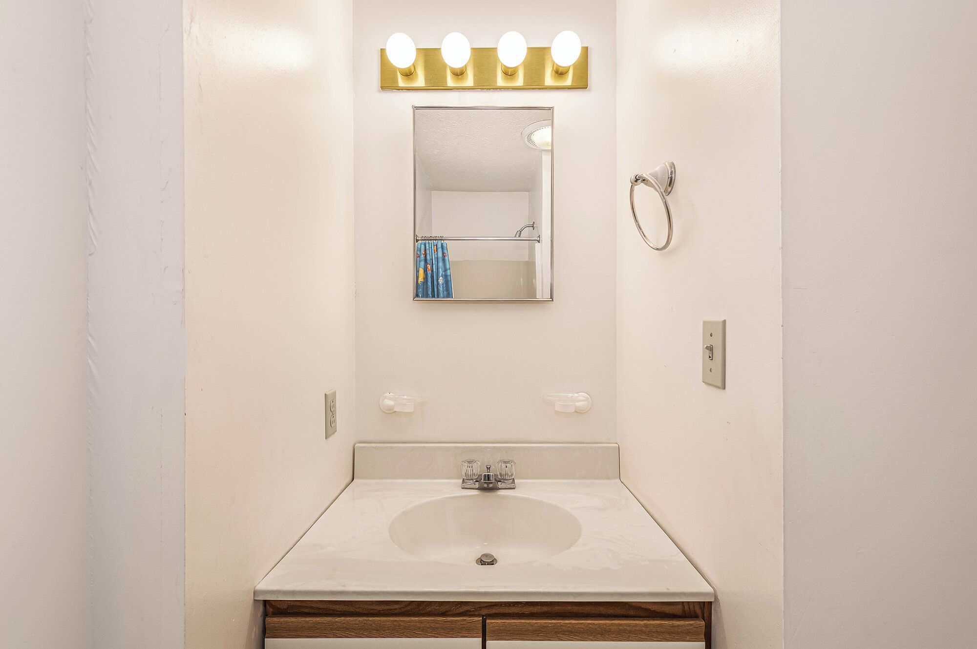 A bathroom with a white sink, a mirror with a gold light strip, and a towel rack.