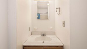 Ein Badezimmer mit einem weißen Waschbecken, einem Spiegel mit goldfarbener Beleuchtung und einem Handtuchhalter.