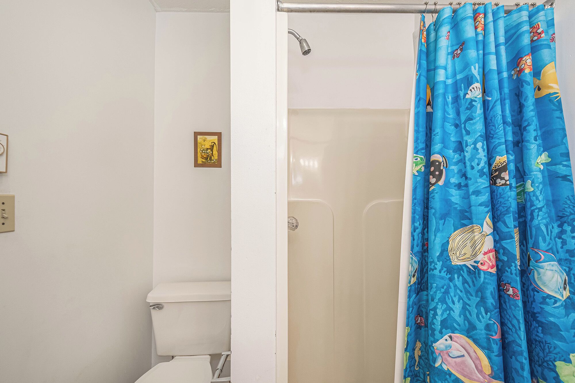 A bathroom with a white toilet, a shower curtain with a marine life pattern, and a small framed picture on the wall.