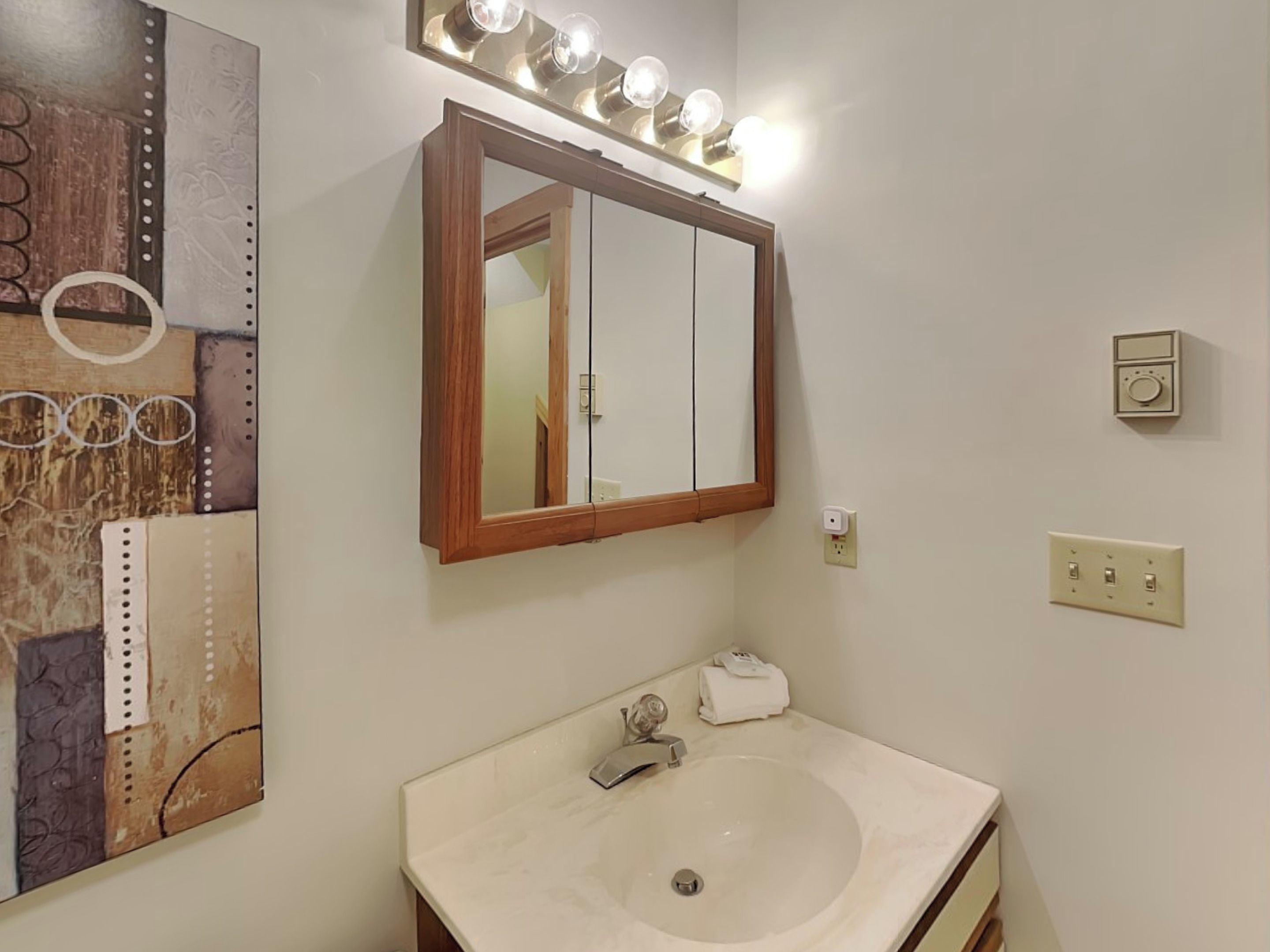 Une salle de bain avec un grand miroir, un meuble-lavabo, un évier et des luminaires au-dessus du miroir.