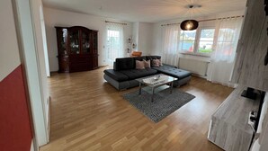 A living room with a sectional sofa, a glass coffee table, and a wooden cabinet.