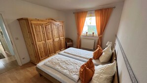 A bedroom with two beds, wooden wardrobe, and a window with curtains.