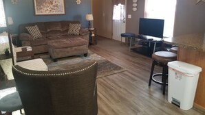 Een woonkamer met een bruine bank, een salontafel, een televisie en een kleine tafel met een lamp.