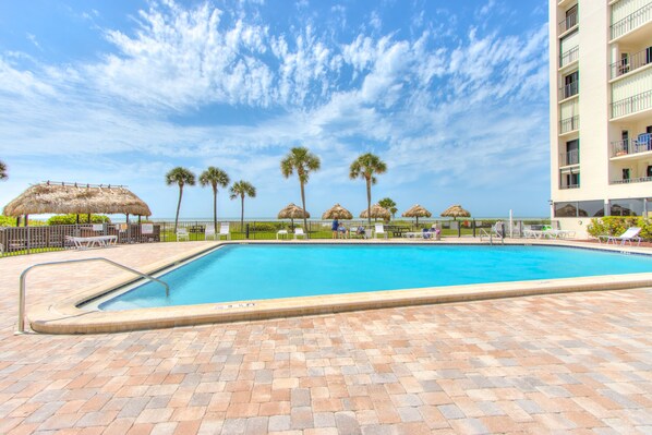 Relax by the pool surrounded by palm trees and shaded by thatched umbrellas.