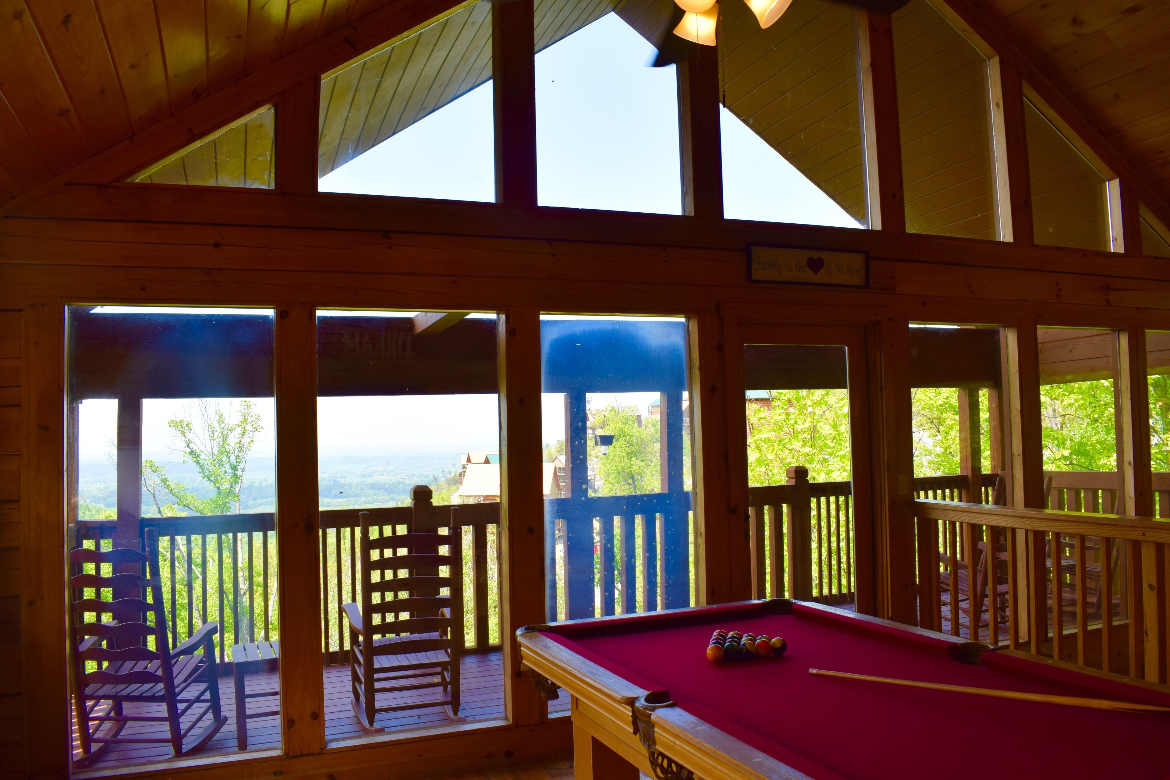 A pool table in a wooden room with large windows and a view of greenery outside.