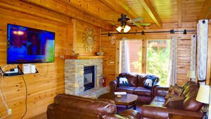 A wooden cabin interior with a stone fireplace, leather furniture, and a television mounted on the wall. - ENCHANTED VIEW~**Super cozy & Awesome Valley Views~10 minutes to Pigeon Forge ** (Sevierville)