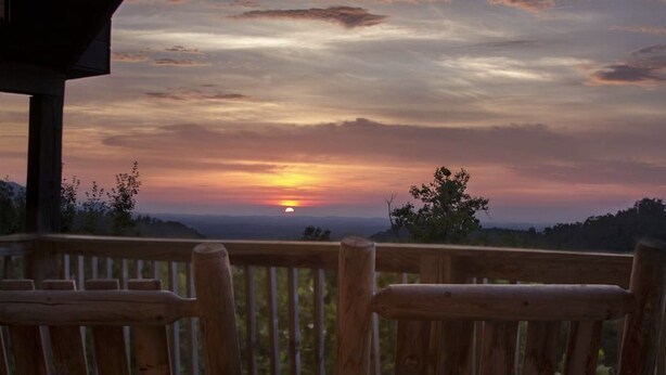 A wooden deck with a view of a sunset over a hilly landscape. - ENCHANTED VIEW~**Super cozy & Awesome Valley Views~10 minutes to Pigeon Forge ** (Sevierville)