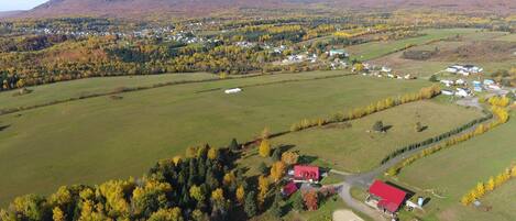 Une vue aérienne d’un paysage rural, avec des maisons dispersées, des champs et un bâtiment imposant dont le toit est de couleur rouge.