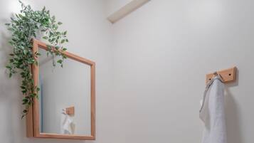 Une salle de bain avec un lavabo blanc, un miroir encadré en bois, un porte-serviettes et une petite étagère en bois où sont posées des serviettes.