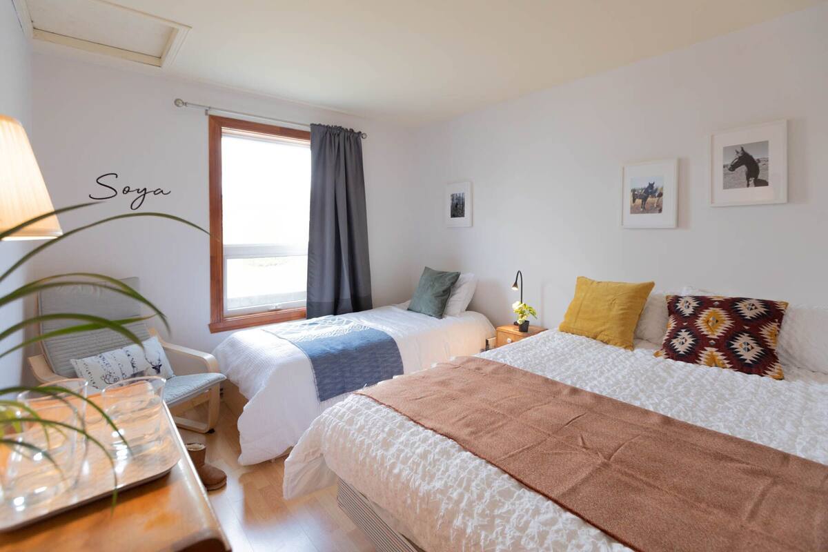 A bedroom with two beds, a desk, a chair, and a window with curtains.