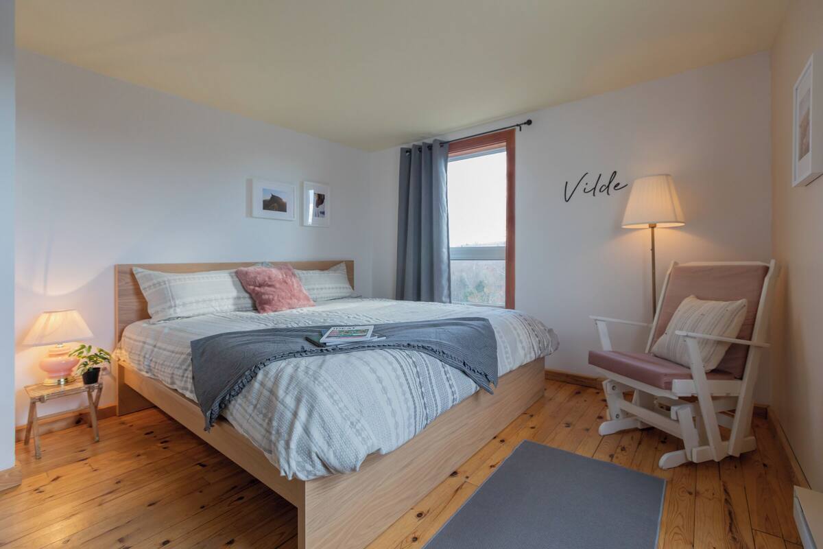 A bedroom with a bed, bedside lamp, chair, and a window with curtains.