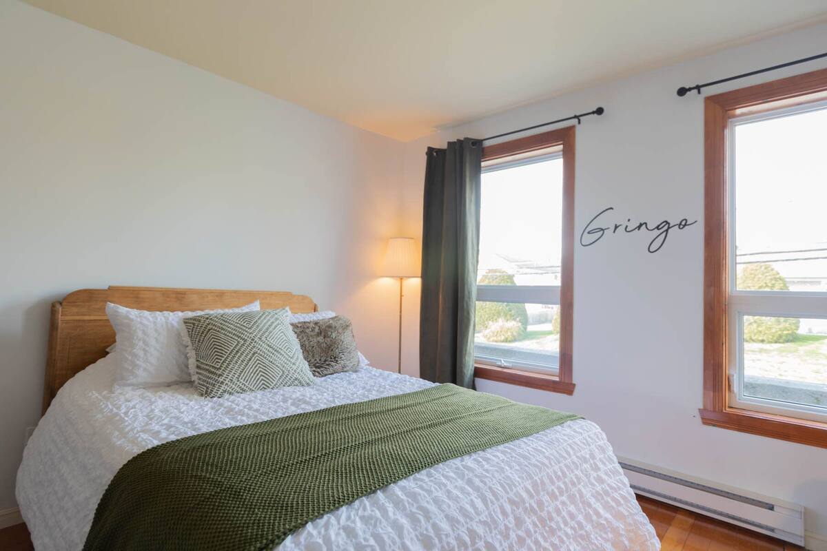A bedroom with a wooden headboard, a green throw blanket, and a white quilted bedspread.