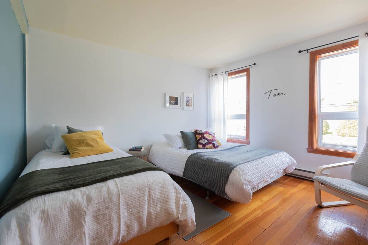 A bedroom with two beds, wooden flooring, a chair, and a window with a view.