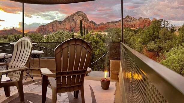 A terrace with outdoor seating, a view of red rock formations, and a sunset.