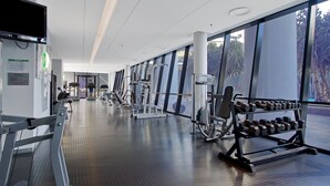A modern gym with various exercise equipment, large windows, and a clean, spacious layout.