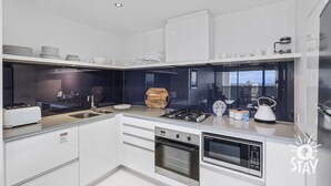 A modern kitchen with white cabinetry, stainless steel appliances, and a view of the city through a large window.