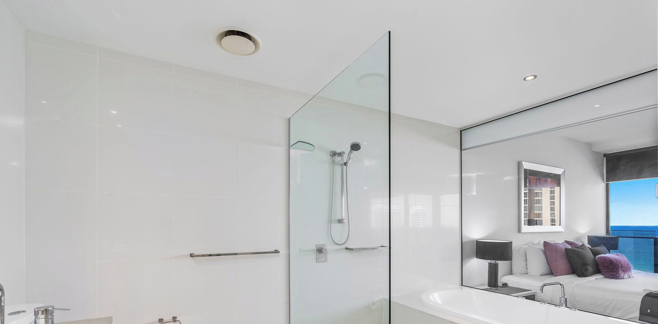 Un baño moderno con ducha envuelta en vidrio, un espejo grande y vista al mar.