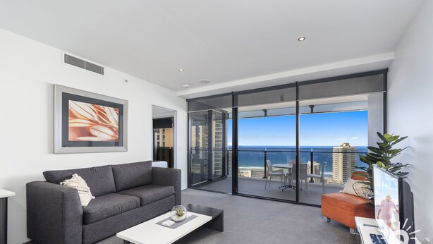 A modern living room with a grey sofa, a white coffee table, and a large window offering a city view.