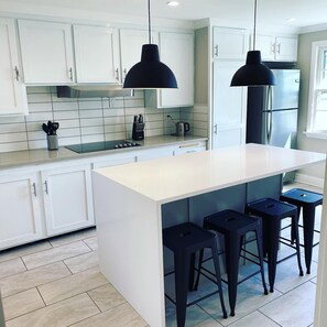 A modern kitchen with white cabinets, a central island with bar stools, a stainless steel refrigerator, and pendant lighting. - Quaint 4 bdr Cape Cod, sleeps 8-10.  4 min to USCGA, Con college & downtown  (New London)