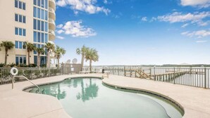 Une piscine à bords incurvés, entourée d’une clôture, et un bâtiment avec des balcons en arrière-plan.