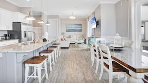 Une cuisine moderne avec des meubles blancs, un grand îlot central doté de tabourets et un éclairage suspendu.
