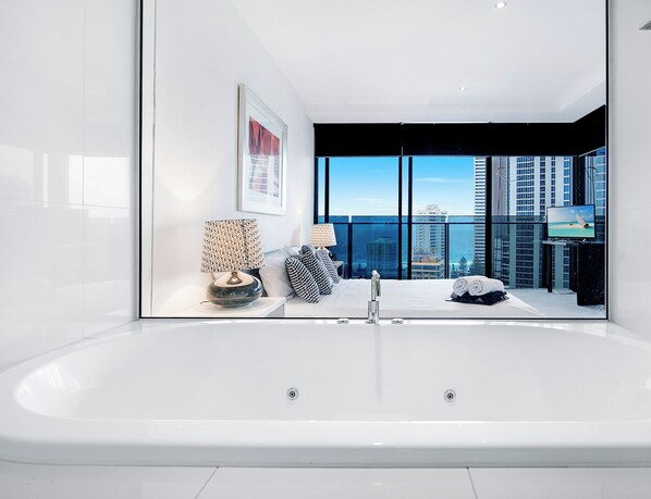 Un baño moderno con una bañera grande, vistas de la ciudad a través de amplias ventanas y una obra de arte enmarcada en la pared.
