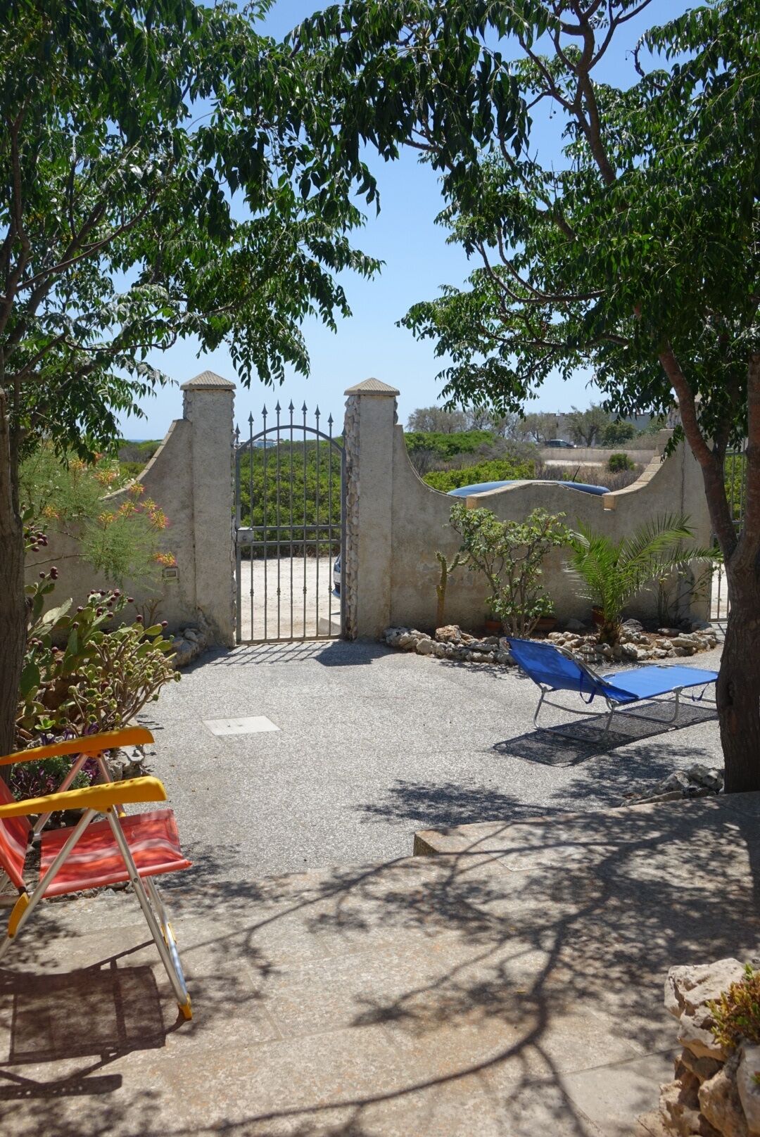 An outdoor area with a paved surface, a metal gate, and two sun loungers.