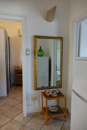 Un pasillo con un espejo en la pared, una pequeña consola de madera con objetos decorativos y un jarrón verde sobre la consola.