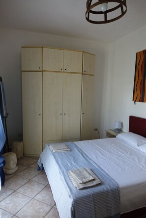 Un dormitorio con cama, armario, lámpara y una obra de arte en la pared.