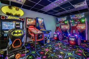 Una sala de juegos recreativos con diversas máquinas, incluyendo un juego con temática de Batman, un juego de carreras y una máquina de premios.
