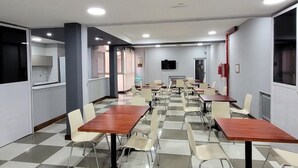 Un salón de conferencias con piso a cuadros, varias mesas y sillas, un televisor y un extintor.
