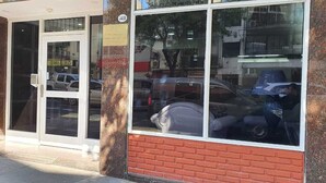 Fachada de ladrillo con puerta de cristal y reflejo de coches estacionados.