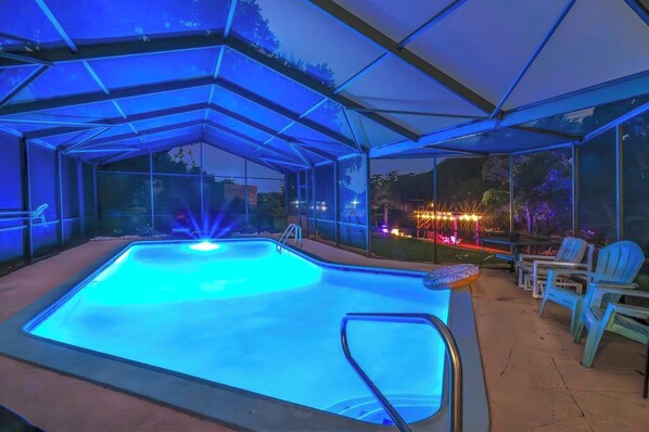 A covered outdoor swimming pool with a glass enclosure, a bar area, and outdoor seating. - 7BR Lakefront | Pool & Hot Tub (Orlando)