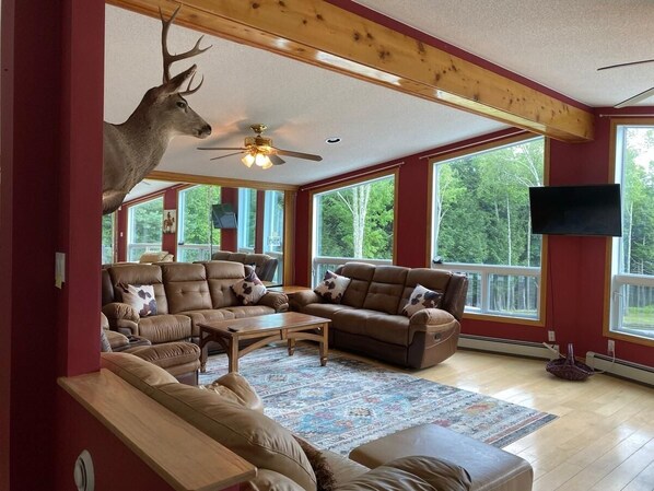 A spacious living room with a ceiling fan, large windows, and a mounted deer head.