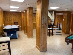 A room with a pool table, a foosball table, and a staircase.