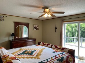 A bedroom with a bed, a dresser, a ceiling fan, a window with a view of trees, and a mirror. - Stunning home 17 acres in the Catskill Mountains (Ashland)
