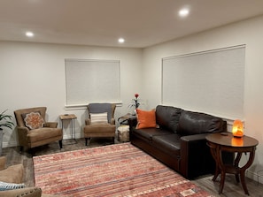 A living room with a brown leather sofa, a brown armchair, a patterned rug, and a small table with a lamp.