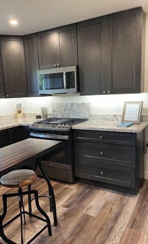 A modern kitchen with dark cabinets, a stainless steel microwave, a gas stove, and a marble countertop.