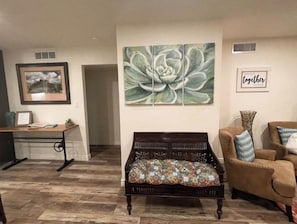 Un salon avec un banc en bois, un tableau encadré, une grande œuvre d’art florale et un panneau portant l’inscription « ensemble ».