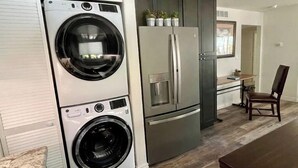 A compact kitchen with a built-in washer and dryer, a stainless steel refrigerator, and a dining area with a wooden table and chairs. - Coffee Pot Rock Views! Equipped with an Electric Vehicle charger. (Sedona)