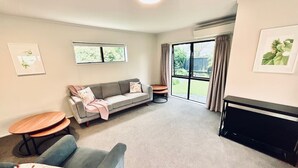 A living room with a sofa, a coffee table, a fireplace, and a large window with curtains. - Aintree On The  Park (Mount Maunganui)