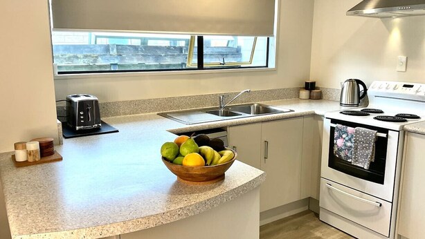 A kitchen with a built-in oven, a sink, and a window above the counter. - Aintree On The  Park (Mount Maunganui)